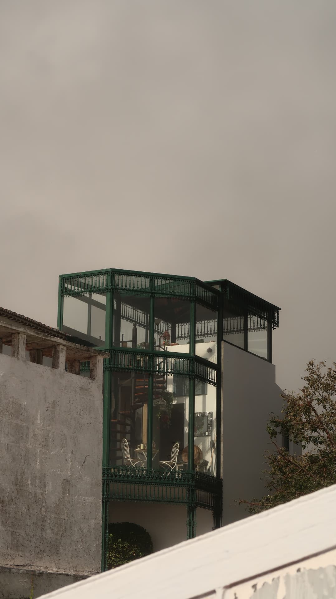 Green-framed glass veranda on a pale building against a hazy sky